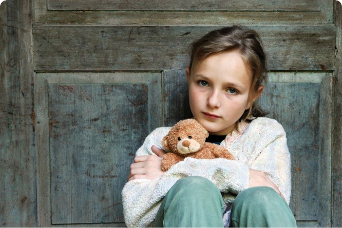 Ein junges Mädchen sitzt vor einer Holztür und hält einen Teddybären, Stepic Charity CEE hilft Kindern.