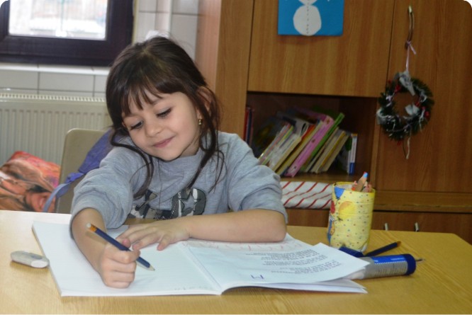 A young girl supported by Stepic Charity CEE writes passionately in a book, highlighting the joy of learning.